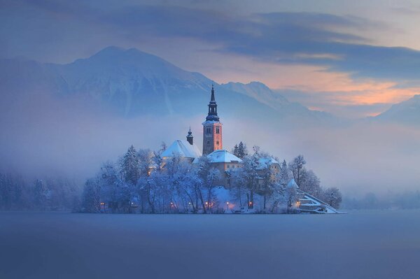 Slowenien. Eine mit Schnee bedeckte Kirche inmitten eines schneebedeckten Feldes. Über Ihr Nebel