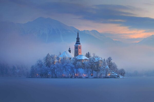 Slovenia. Chiesa coperta di neve in mezzo a un campo innevato. Nebbia sopra di lei