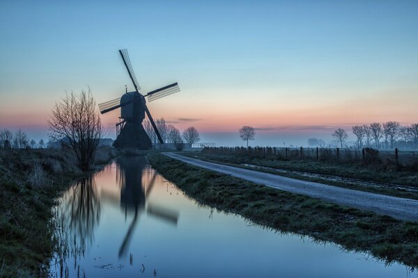 Windmill and road by the water, against the background of sunset