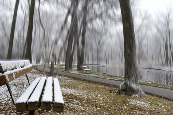 Verschneite Bank im Park am Teich