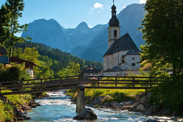 Ponte sul fiume tra alberi, montagne, Chiesa