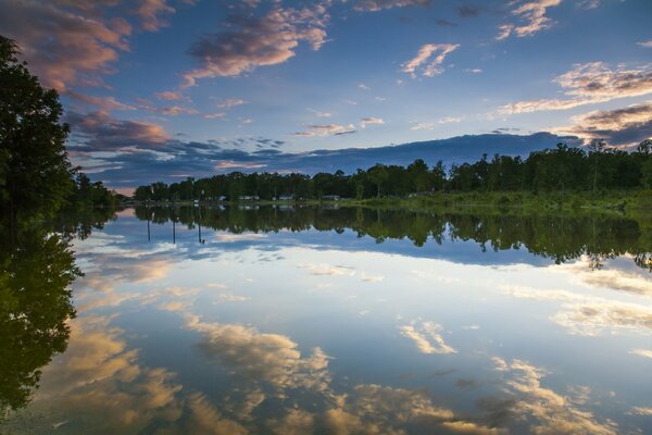 Die Wasseroberfläche mit der Reflexion des Himmels. Abend. Die Reflexion der Wolken im Wasser. Wald am Ufer