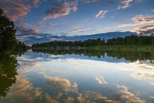 Superficie de agua con el reflejo del cielo. Noche. Reflejo de las nubes en el agua. Bosque en la orilla