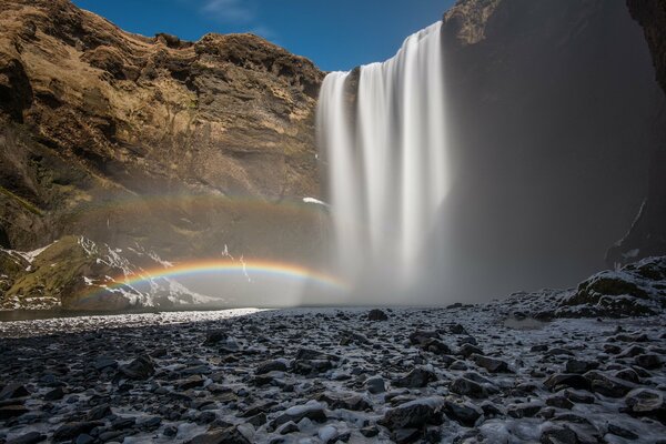 Wasserfall und Regenbogen auf blauem Himmel Hintergrund