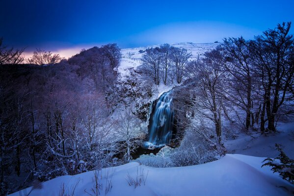 Winter landscape with snow-covered trees and waterfall