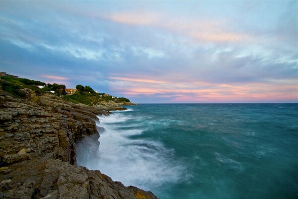 Blau-rosa Wolken über Felsen und Meer