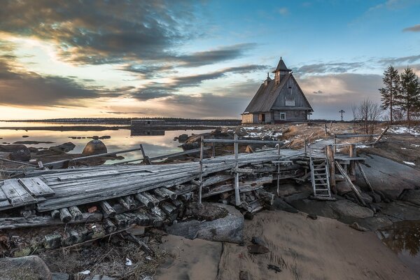 Eine hölzerne Kirche. Holzbrücke. Sonnenuntergang am Fluss