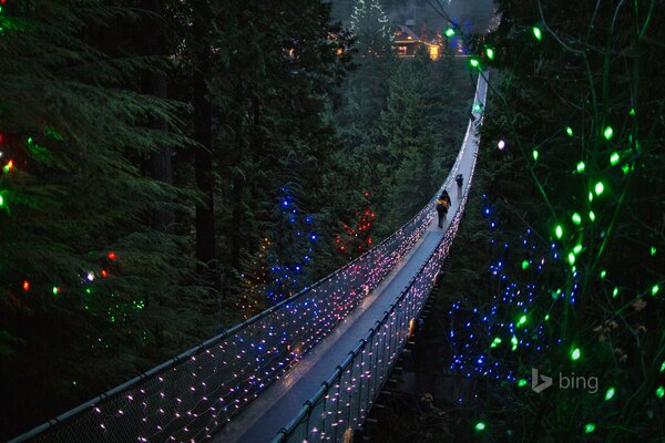 Le persone attraversano un ponte sospeso con luci natalizie