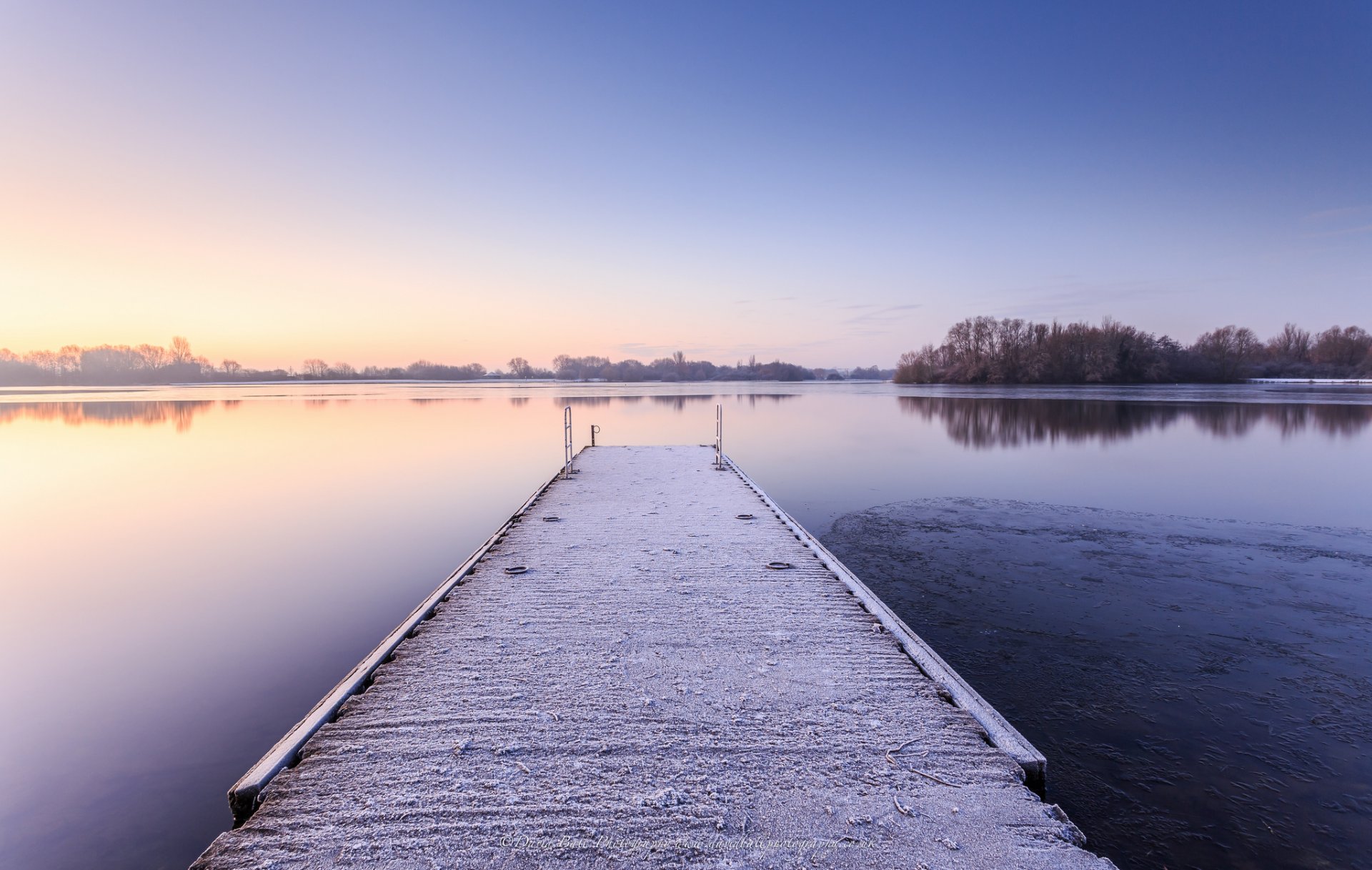 united kingdom england winter morning lake water surface of next beach bridge snow tree reflection