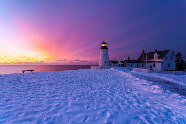 Indescribable winter in England of the Bristol lighthouse, snow-white snow, sunset, a bench on the shore, footprints to the structure