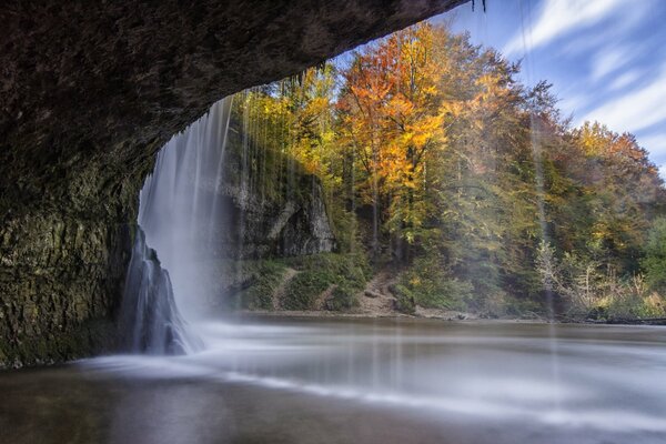 Im Herbst fällt ein Wasserfall von einer Klippe in den See