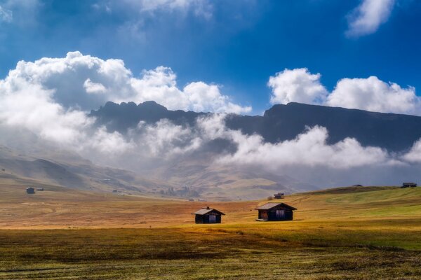 In the valley there are two houses against the background of huge mountains