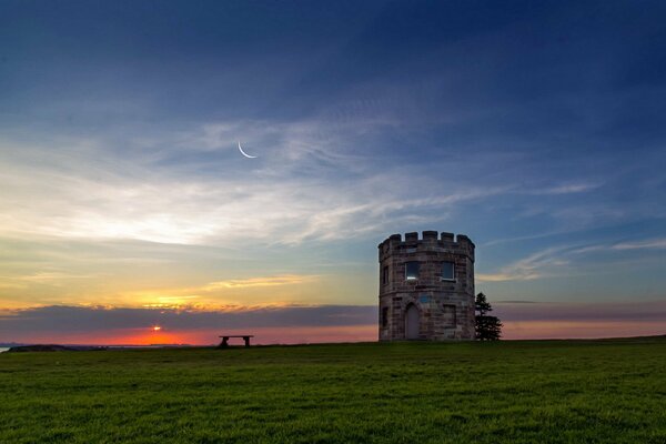 Al atardecer fotografiado el campo y el banco con la torre