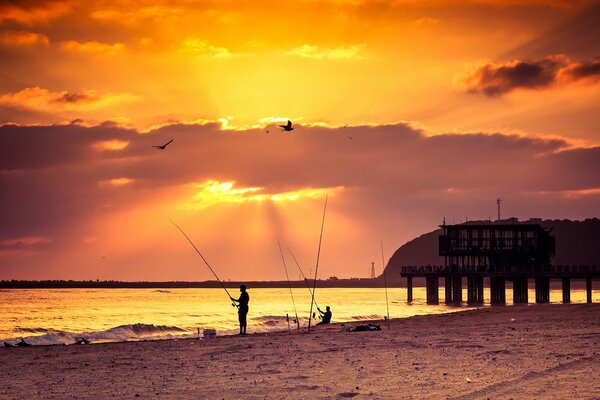 Tramonto in riva al mare. Uomo che pesca sulla riva