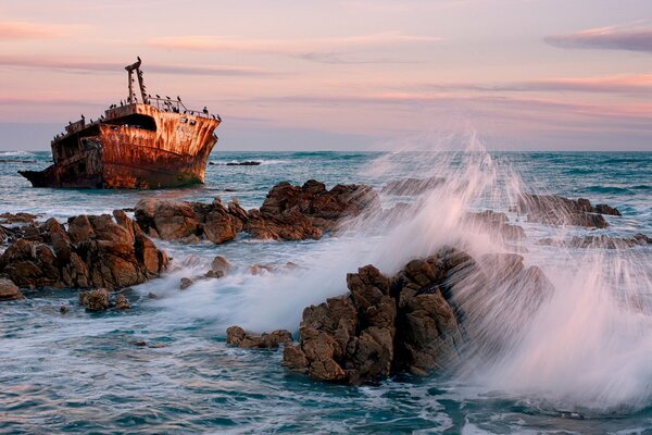 Navire au milieu de la mer et des rochers sur fond de coucher de soleil