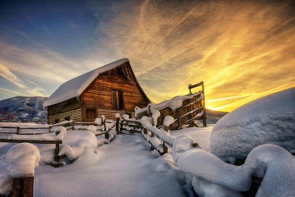 Maison dans la neige sur fond de coucher de soleil et de congères