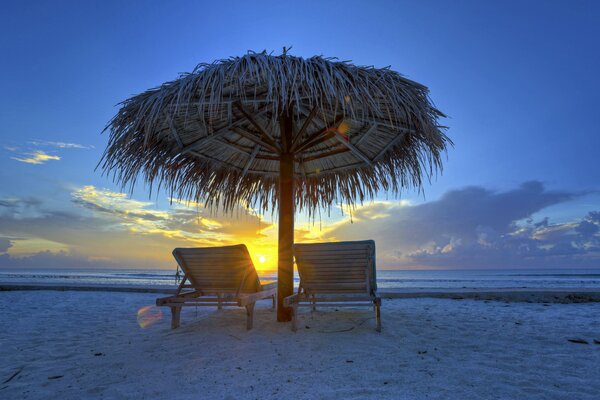 Sun loungers under an umbrella against the sunset