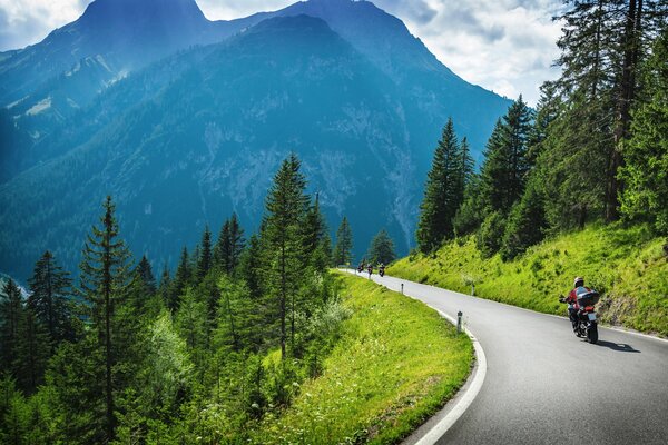 Un motocycliste roule sur une piste de montagne parmi les montagnes vertes